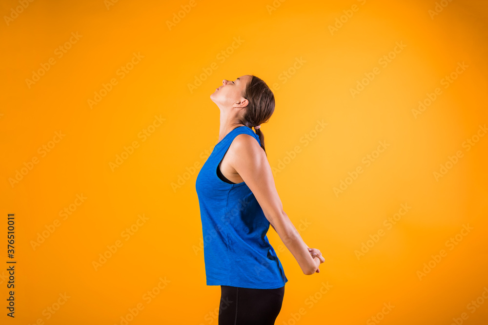 a beautiful woman in a sports uniform does a neck warm-up on an orange isolated background - obrazy, fototapety, plakaty 