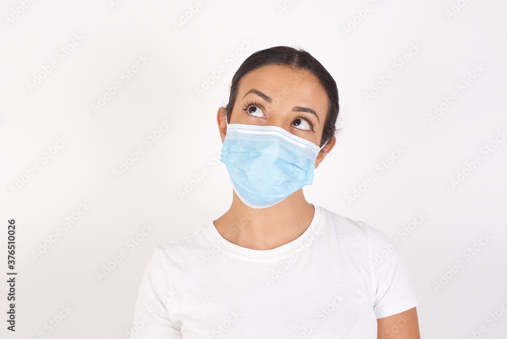 Young arab woman wearing medical mask standing over isolated white background, looking aside into empty space thoughtful Young arab woman wearing medical mask standing over isolated white background, looking aside into empty space thoughtful