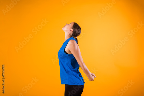 a beautiful woman in a sports uniform does a neck warm-up on an orange isolated background