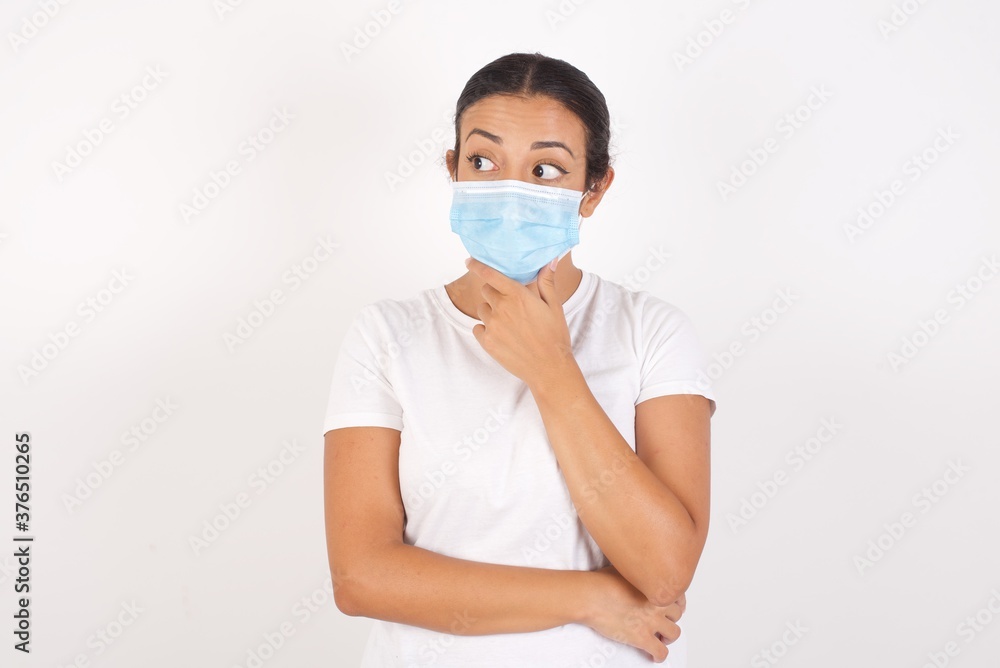 Young arab woman wearing medical mask standing over isolated white background Thinking worried about a question, concerned and nervous with hand on chin.