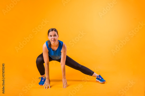 a young woman in a sports uniform performs squats on an orange background