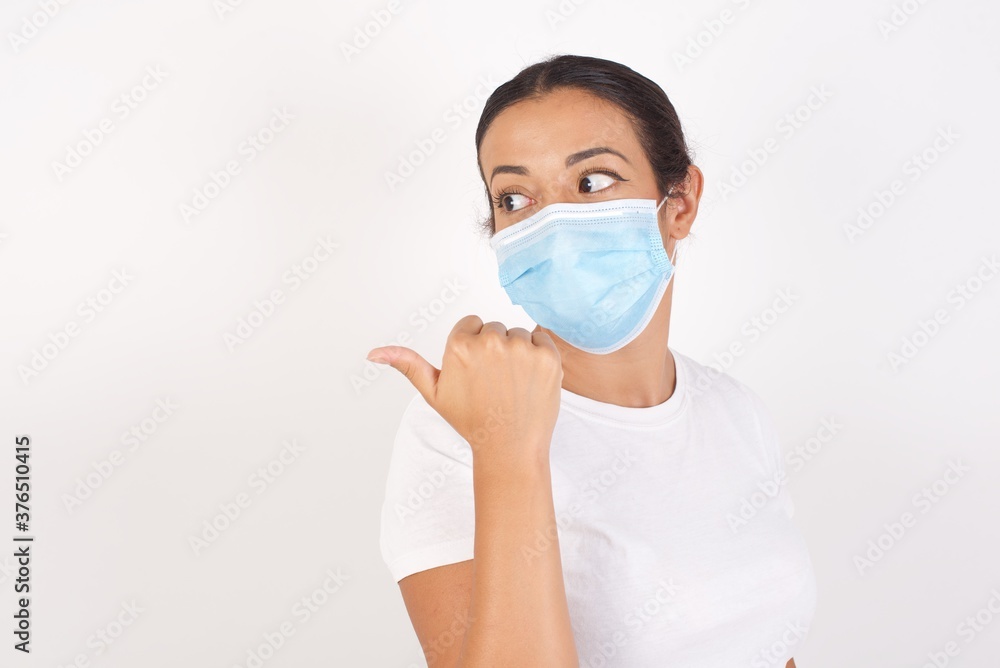 charming Young arab woman wearing medical mask standing over isolated white background, looking aside and indicaring finger side empty space charming Young arab woman wearing medical mask standing over isolated white background, looking aside and indicaring finger side empty space