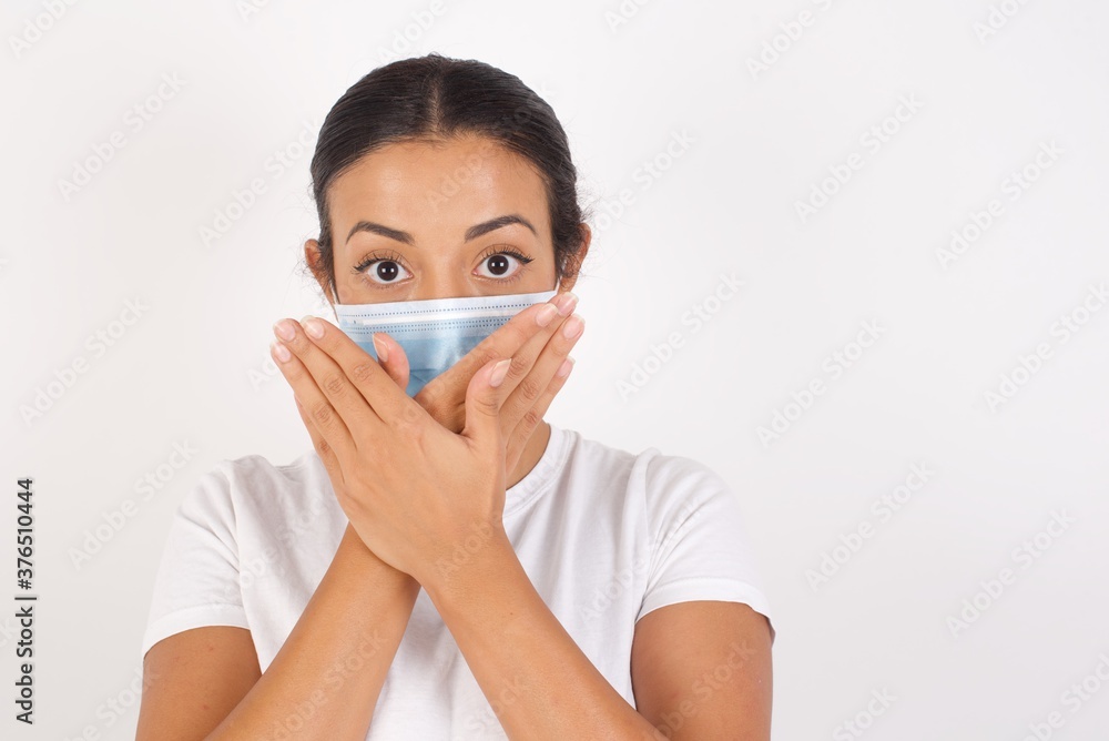 Young arab woman wearing medical mask standing over isolated white background shocked covering mouth with hands for mistake. Secret concept. Young arab woman wearing medical mask standing over isolated white background shocked covering mouth with hands for mistake. Secret concept.