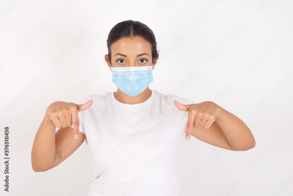 Young arab woman wearing medical mask standing over isolated white background pointing with two fingers at copy space down. Place for advertising Young arab woman wearing medical mask standing over isolated white background pointing with two fingers at copy space down. Place for advertising