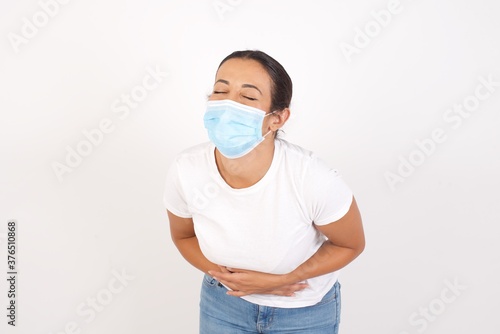 Young arab woman wearing medical mask standing over isolated white background smiling and laughing hard out loud because funny crazy joke with hands on body. © Roquillo