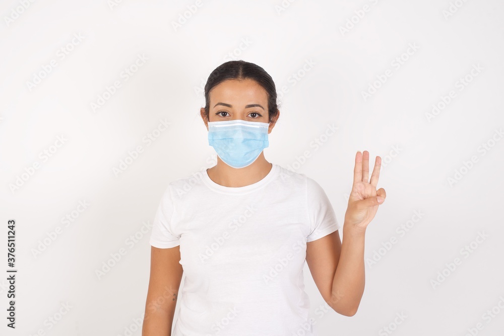 Young arab woman wearing medical mask standing over isolated white background showing and pointing up with fingers number three while smiling confident and happy. Young arab woman wearing medical mask standing over isolated white background showing and pointing up with fingers number three while smiling confident and happy.