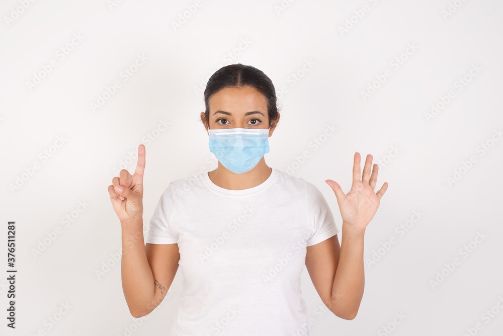 Young arab woman wearing medical mask standing over isolated white background showing and pointing up with fingers number six while smiling confident and happy. Young arab woman wearing medical mask standing over isolated white background showing and pointing up with fingers number six while smiling confident and happy.