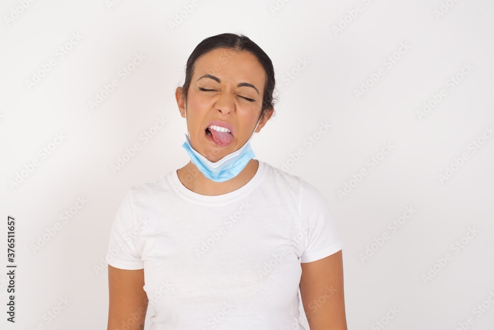 Young arab woman wearing medical mask standing over isolated white background sticking tongue out happy with funny expression. Emotion concept. Young arab woman wearing medical mask standing over isolated white background sticking tongue out happy with funny expression. Emotion concept.
