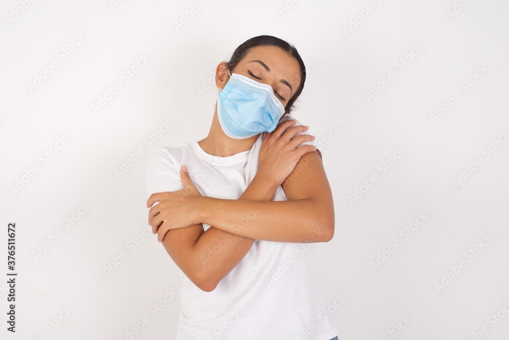 Young arab woman wearing medical mask standing over isolated white background Hugging oneself happy and positive, smiling confident. Self love and self care