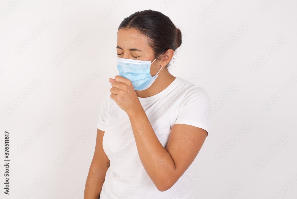 Young arab woman wearing medical mask standing over isolated white background feeling unwell and coughing as symptom for cold or bronchitis. Healthcare concept.
