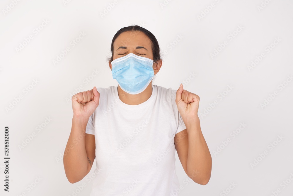 Young arab woman wearing medical mask standing over isolated white background being excited for success with raised arms and closed eyes celebrating victory. Winner concept.