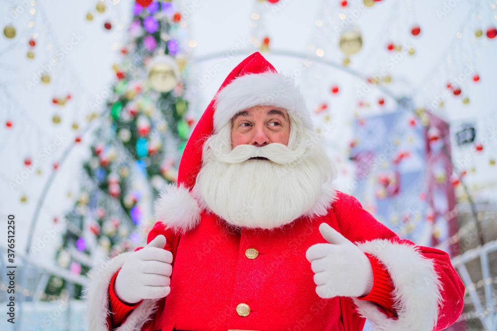 Portrait of an elderly man dressed as santa claus on the background of a christmas tree outdoors. Portrait of an elderly man dressed as santa claus on the background of a christmas tree outdoors.