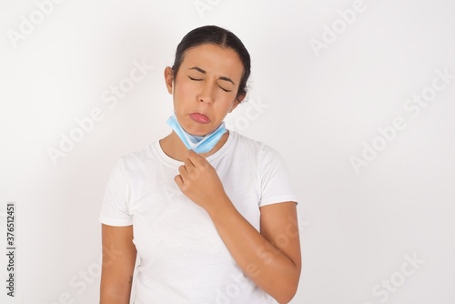 Dismal gloomy rejected Young arab woman wearing medical mask standing over isolated white background has problems and difficulties, curves lower lip and closes eyes in despair, being in depression 