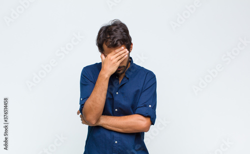 young latin handsome man looking stressed, ashamed or upset, with a headache, covering face with hand