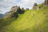 Two hikers walking on a path in Quiraing, Isle of Skye, Scotland, on sunny day. Beautiful area of grassy mountains covered by blooming heather in summer, hidden lochs and steep cliffs