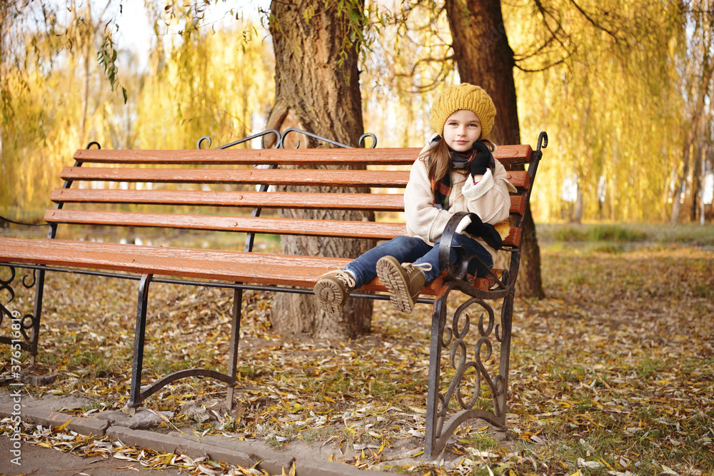 Cheerful preschooler little girl in coat and yellow hat with autumn