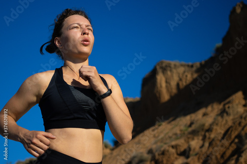 Young sport woman in black sportswear trail running marathon, breathing heavily in amazing mountain nature landscape and blue sky. Training for triathlon run and active lifestyle concept. Copy space