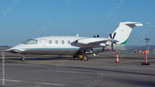 Side view of white business airplane with twin turboprop engines mounted in pusher configuration. Blue sky over the airport. Modern technology in fast transportation, business travel and tourism. 