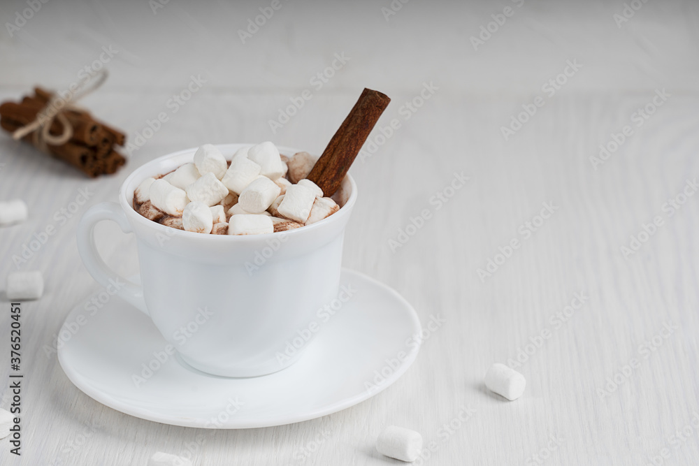 Cup full of hot homemade cacao drink usually prepared at cold winter and autumn seasons served on plate with marshmallows and cinnamon on white wooden background. Image with copy space, horizontal Cup full of hot homemade cacao drink usually prepared at cold winter and autumn seasons served on plate with marshmallows and cinnamon on white wooden background. Image with copy space, horizontal