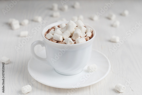 Hot aromatic homemade cacao drink with marshmallow usually cooked at cold autumn and winter vacations served on plate on white wooden background at kitchen. Horizontal orientation image