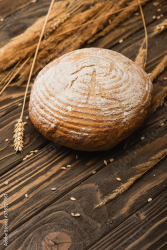 selective focus of fresh baked white bread loaf with spikelets on wooden surface
