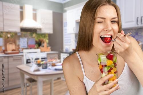 Young woman eating fruits from glass on blurred kitchen background