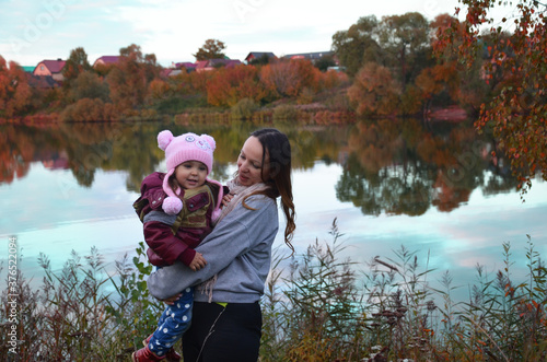 mom and daughter walk by the lake in autumn. Against a background of autumn colours and leaves, a mother smiling next to her daughter. The trees are reflected in the lake. photo