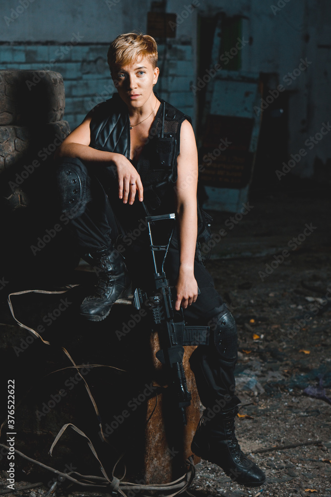 Naklejka premium Portrait of young woman soldier in black uniform with a rifle posing to the camera.