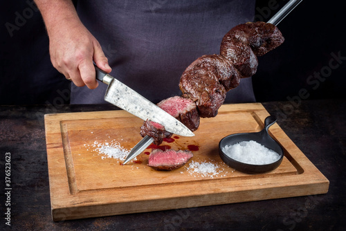 Traditional barbecue dry aged wagyu Brazilian picanha from the sirloin cap of rump beef sliced by a chef directly from the skewer as close-up on a wooden cutting board photo