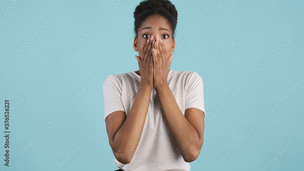 Attractive shocked casual african american girl emotionally covering face with hands on camera over colorful background Attractive shocked casual african american girl emotionally covering face with hands on camera over colorful background