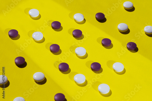 Different white and purple pills on a bright yellow surface, health relating background