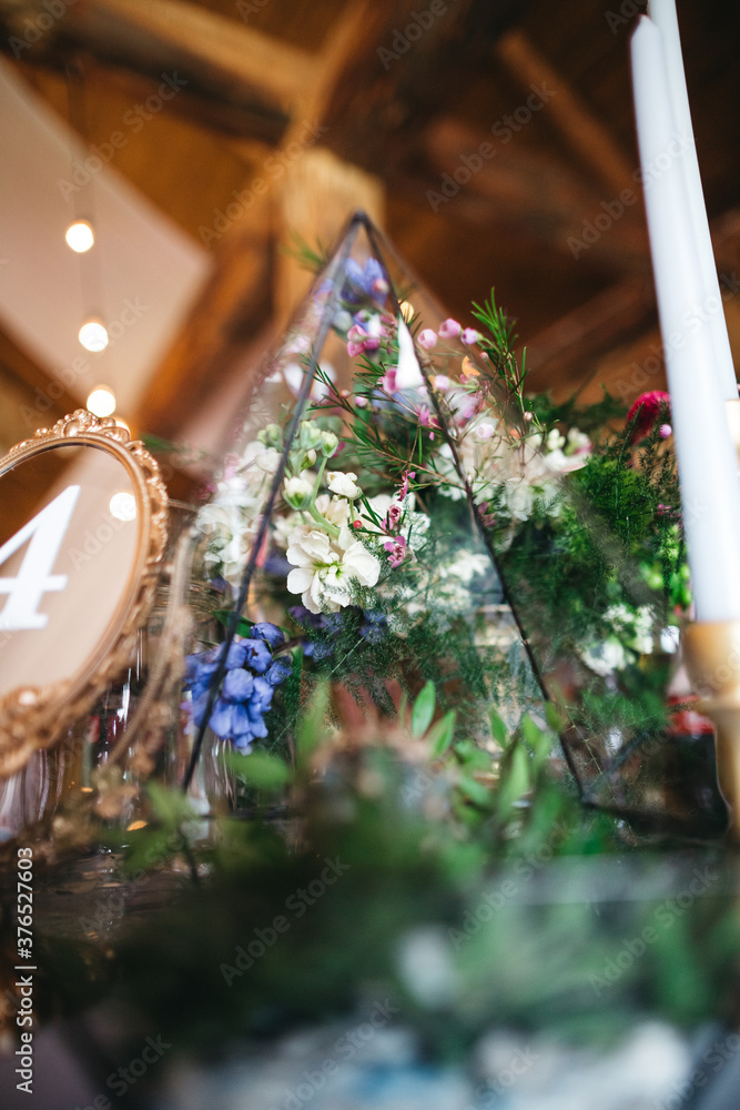 Konstfotografi Close up of floral composition of fresh colorful flowers in glass florarium on restaurant table with table number four and candle