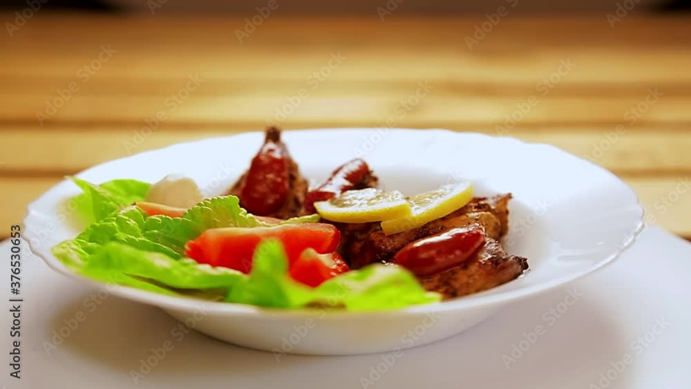A white plate with pieces of meat grilled on lettuce leaves with ketchup and lemon and cherry is rotating in a circle. A white plate with pieces of meat grilled on lettuce leaves with ketchup and lemon and cherry is rotating in a circle.