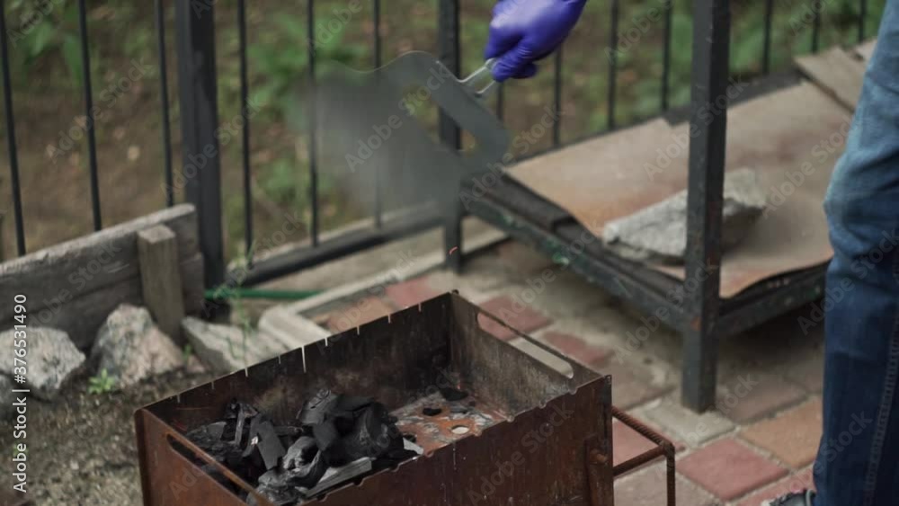 guy in jeans makes fire for barbecue in medical gloves. man inflates coals, sparkles. Coals in brazier. hand shakes shovel over coals. Cooking dinner in backyard village, on self-isolation quarantine. guy in jeans makes fire for barbecue in medical gloves. man inflates coals, sparkles. Coals in brazier. hand shakes shovel over coals. Cooking dinner in backyard village, on self-isolation quarantine.
