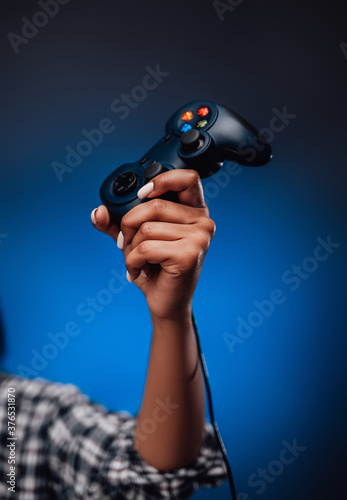 Gaming sport hobby and modern quality device in foggy blue background. Blackskinned female hand holding joystick and pointing it up. photo