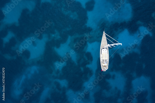 View from above, stunning aerial view of a white sailboat, floating on a turquoise, clear water. Sardinia, Italy. Sardinia is the second-largest island in the Mediterranean Sea. © Travel Wild