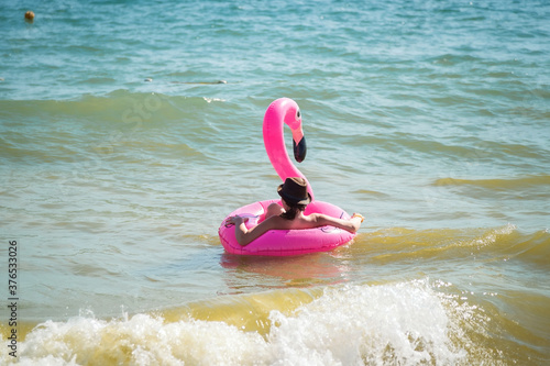 A girl swims in the sea on an inflatable pink Flamingo. Swimming on the waves. Black sea coast.