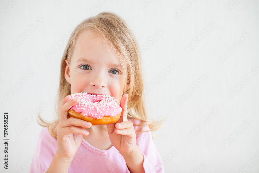 Little happy girl with blond hair playing and tasting donuts with pink icing at hanukkah celebration
