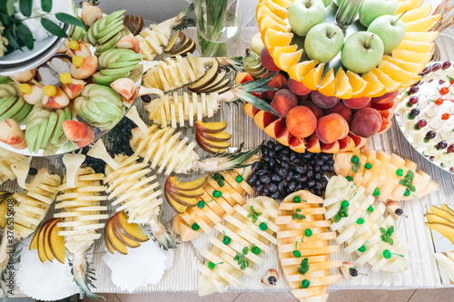 Top view of sliced and decorated trays with fresh fruits on table on wedding buffet. Delicious green apples, pineapple, grapes, peaches on birthday sweet bar, all inclusive. Concept of luxury life.