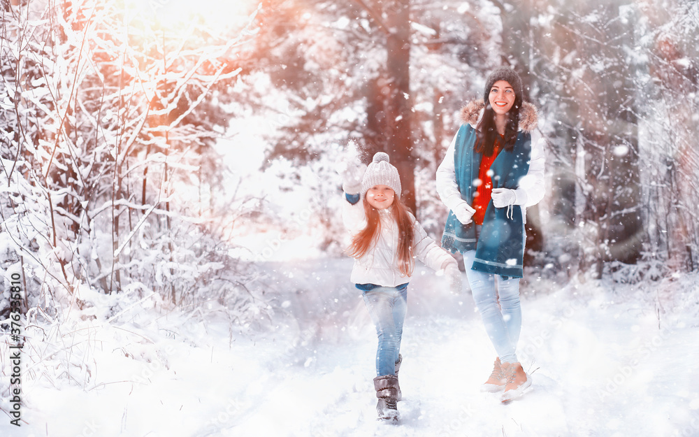 Fototapeta premium Young family for a walk. Mom and daughter are walking in a winter park.
