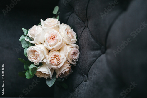 Front view of beautiful wedding bouquet for bride made of pale orange roses on grey sofa. Lying pretty bouquet  preparing for romantic date  anniversary floral surprise. Concept of tender love gifts.