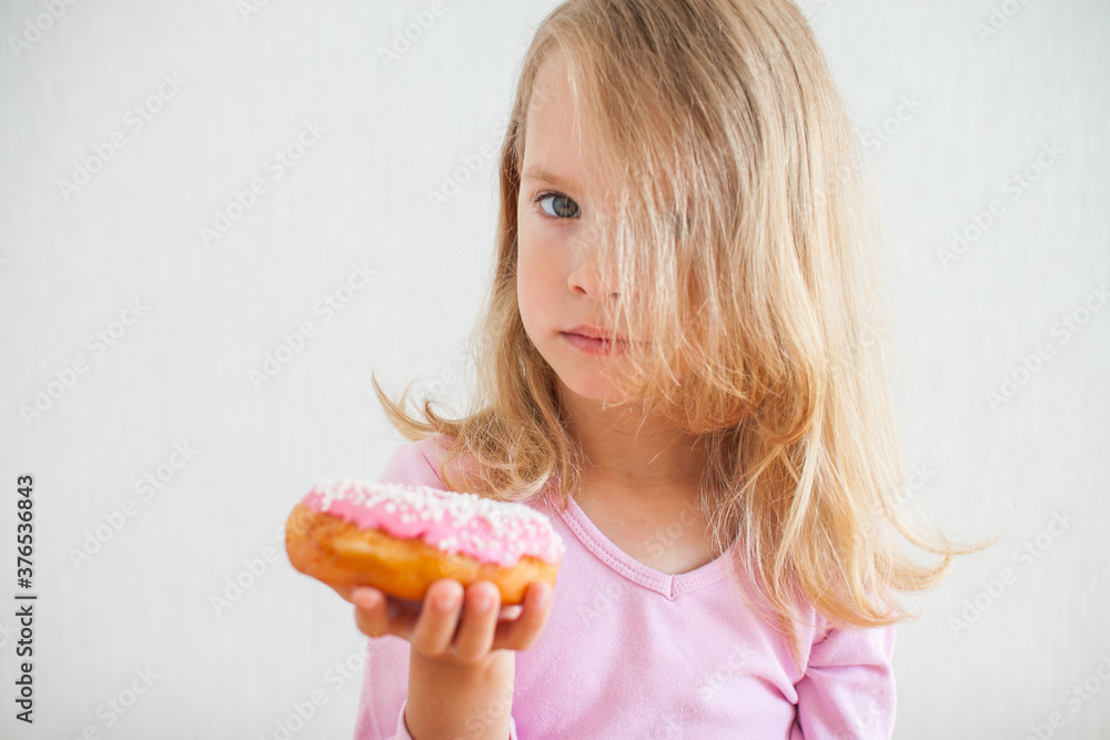 Little happy girl with blond hair playing and tasting donuts with pink icing at hanukkah celebration