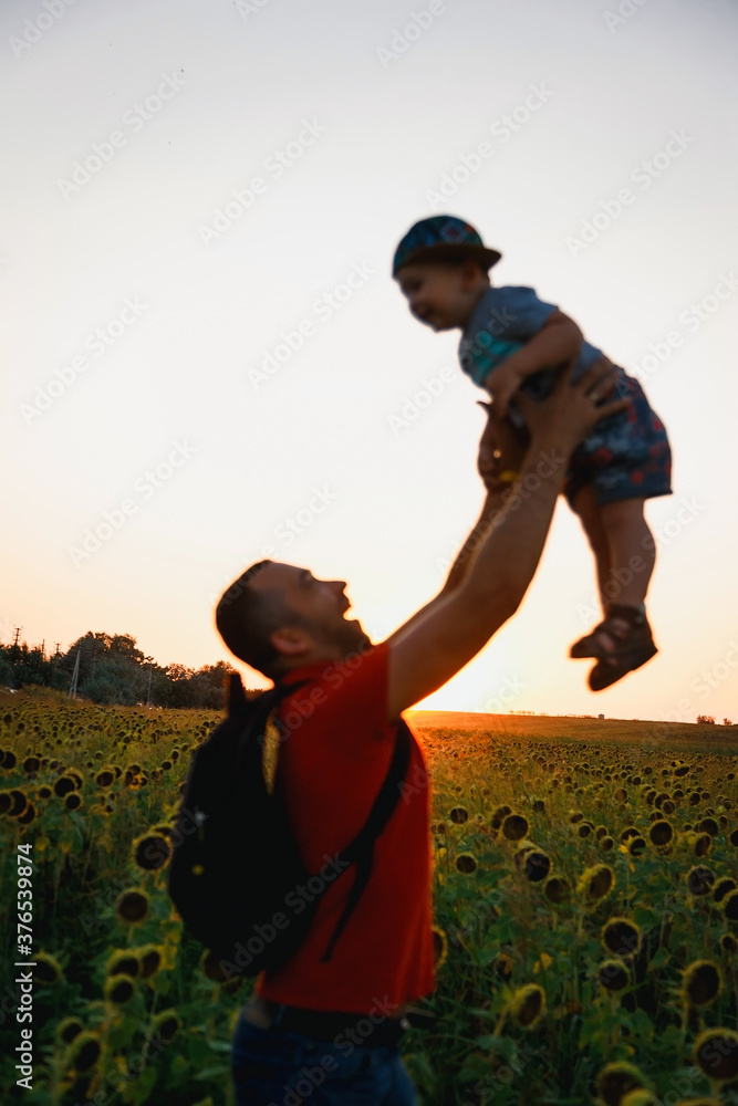 A father with his son in his arms in nature. Figures of people on the background of the sunset.