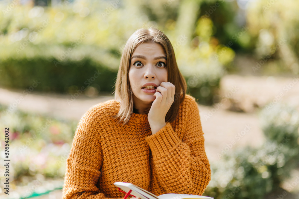 Worried woman reading on blur background. Outdoor shot of funny girl in sweater holding book. Worried woman reading on blur background. Outdoor shot of funny girl in sweater holding book.