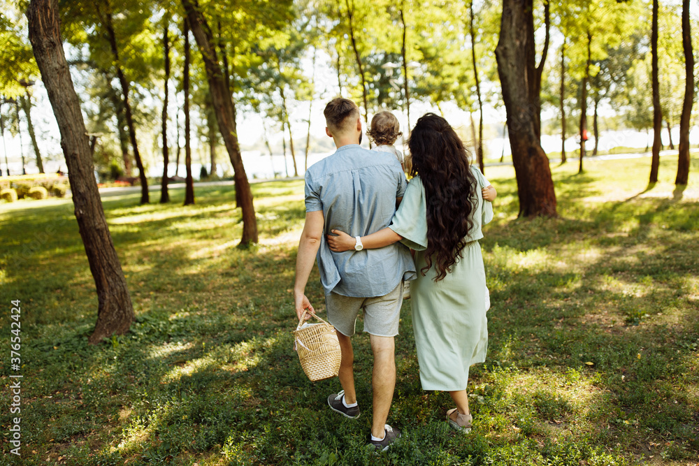 Fototapeta premium Happy parents with little children walking at the park, caring mother hold in arms cute son, beautiful daughter sitting in father hands, family weekend, parenting concept