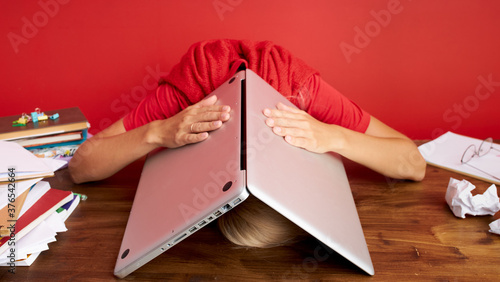 portrait of a young caucasian woman holding laptop computer on his head, deadline at work, frustration concept, being fired from job dismissed at work due to economic crisis and recession photo