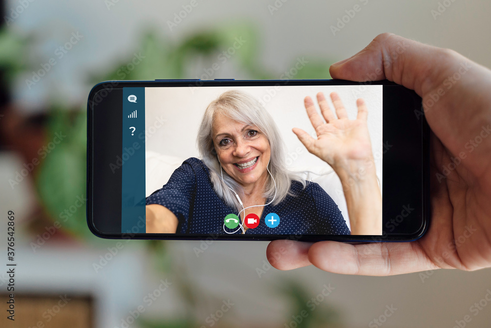 Happy senior woman making video call meeting on smart phone at work from home - Cheerful old female waving at screen on virtual webinar videocall - Elderly and technology concept - focus on phone