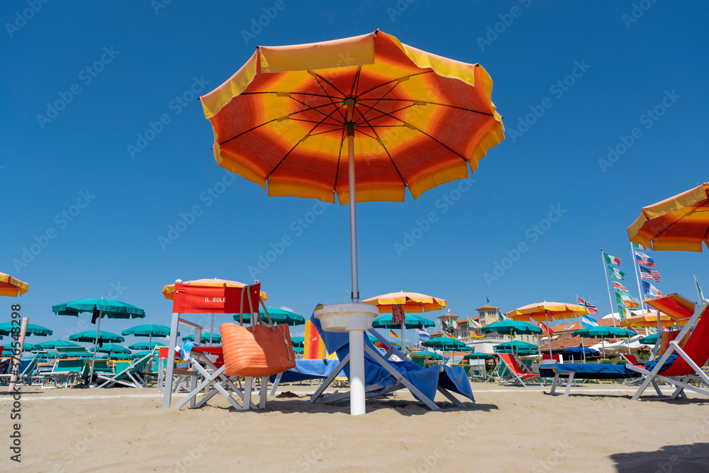 A lot of orange white sun umbrellas on a beach, with a view of a horizon line over the sea