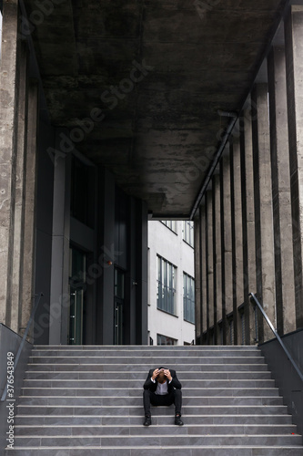 Depressed fired office worker sitting on stairs near modern business center © Ivan