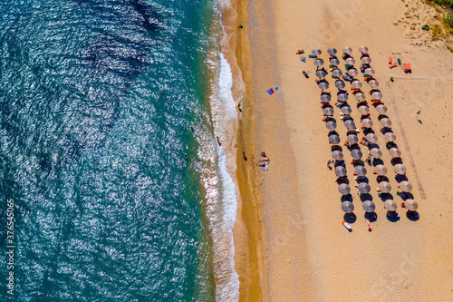View from above, stunning aerial view of an amazing beach with beach umbrellas and turquoise clear water. Top view on sun loungers under umbrellas on the sandy beach. Concept of summer vacation.